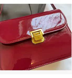 Macro detail of wine red patent leather handbag with textured golden metal clasp