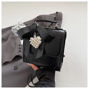 Detail of black patent leather bow bag featuring a pearl heart charm and textured finish