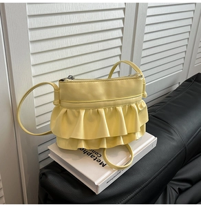 Detail of bright yellow ruffled leather crossbody bag placed on a white book decor