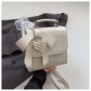 Detail of off-white bow handbag with pearl heart charm and textured synthetic leather