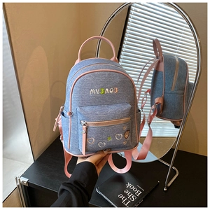 Detail view of denim backpack showing floral embroidery and pink faux leather accents