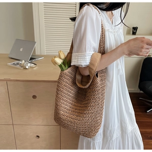 Detailed side view of large brown straw woven tote bag worn over the shoulder