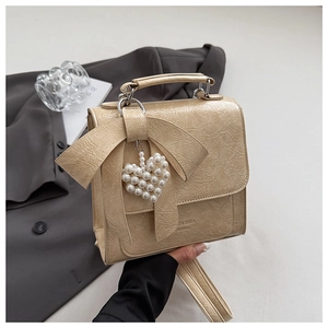 Detail of cream pleated leather crossbody bag with a bow and pearl heart charm