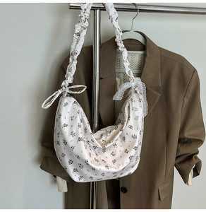 Close-up of crescent bag featuring floral print and ruffled handle with lace bow detail