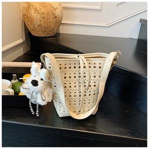 Détail du sac seau beige ajouré avec un pendentif décoratif en forme de petit chien en peluche