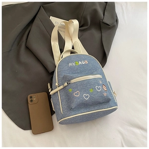 Detail of a mini blue denim backpack with heart embroidery and beige zipper accents