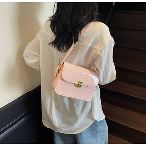 Detail shot of light pink patent leather crossbody bag with golden metal buckle on a model