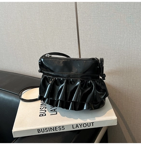 Detail view of black glossy ballet-style shoulder bag with elegant ruffle layers
