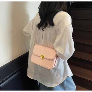 Detail of pink faux leather crossbody bag with square gold metal clasp on a white shirt