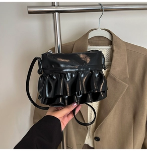 Detail of black patent leather crossbody bag featuring stylish double ruffled decorations