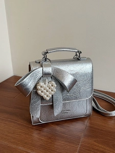 Silver metallic bow handbag with heart pearl charm and long handle on wood floor