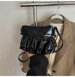 Detail of a black ruffled crossbody bag with a glossy finish and silver zipper closure