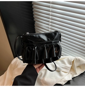 Detail view of the black glossy leather crossbody bag with pleated ruffle trim design