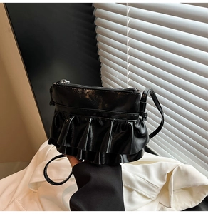 Detail of black glossy leather crossbody bag featuring stylish double ruffled layers
