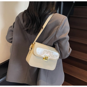 Detail of a beige patent leather crossbody bag featuring a golden square metal lock buckle