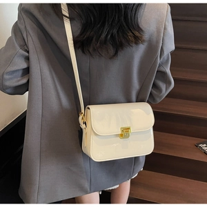 Detail of a creamy white crossbody bag with a gold metal push lock on a dark blazer