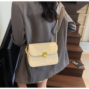 Detail of cream patent leather crossbody bag with gold buckle worn with a grey blazer