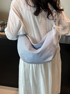 Blue and white striped oxford fabric crescent crossbody bag with bow detail on white dress