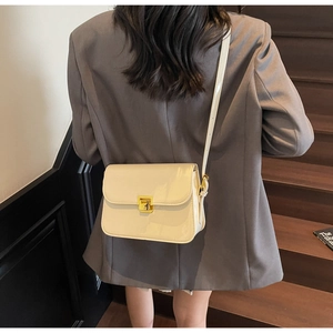 Detail of cream patent leather crossbody bag with a glossy finish and gold metal buckle