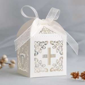 Macro shot of ivory laser-cut cross favor box with delicate white organza bow detail