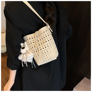 Détail du sac seau beige ajouré avec pendentif en peluche sur un blazer noir chic