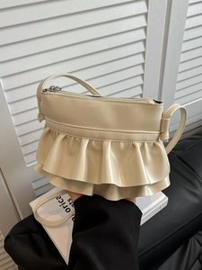 Chic cream ruffled crossbody bag with silver zipper and slim strap on leather background