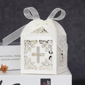 Detailed laser-cut ivory cross favor box with pearlescent finish and white ribbon bow