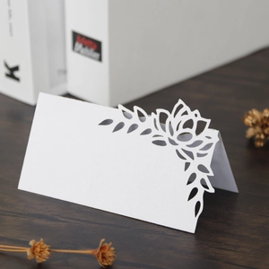 Close-up of laser-cut white cardstock place card with floral hollow pattern on wood