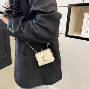 Cream mini kiss-lock bag with silver moon detail and chain strap worn by model