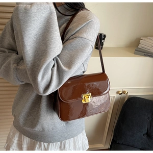 Detail of a dark brown glossy patent leather crossbody bag with a golden square lock