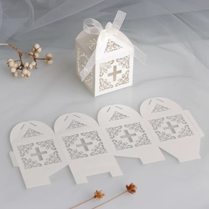 Detail of laser-cut cross candy box with ivory patterns and white silk ribbon
