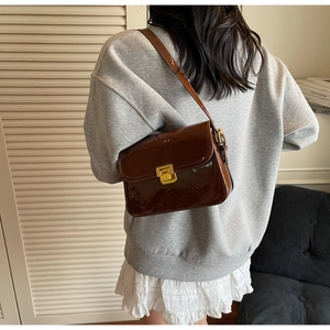Close-up of brown patent leather shoulder bag featuring a gold square buckle and glossy finish