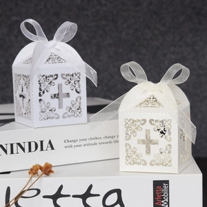 Detail of laser-cut cross pattern candy boxes with elegant organza ribbons in ivory white