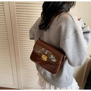 Detail of dark brown glossy patent leather shoulder bag with gold square metal clasp