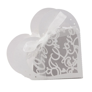 Macro view of white heart-shaped wedding favor box with laser-cut Love text and ribbon