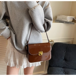 Detailed view of brown patent leather shoulder bag with gold clasp on a model