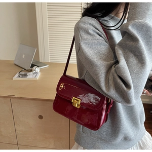 Detail of burgundy patent leather shoulder bag with polished gold square metal buckle