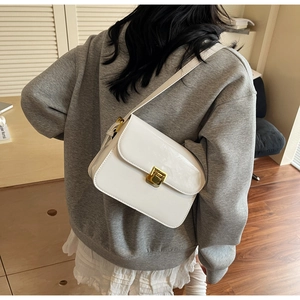 Detail of white glossy patent leather handbag with gold metal clasp on a crossbody strap