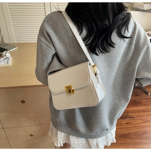 Detail of white glossy shoulder bag with gold square buckle shown on model in warm studio