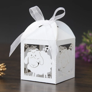 Detailed laser-cut white sheep candy box with elegant organza ribbon on dark wood
