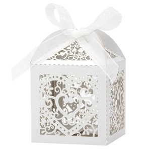 Detail of white laser-cut heart favor box with elegant floral hollow pattern and ribbon bow