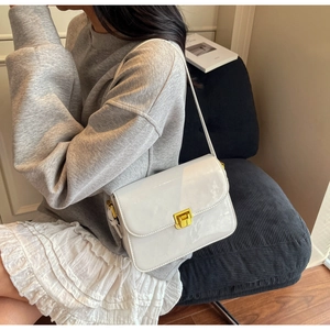 Close-up of a white glossy patent leather shoulder bag with a gold metal twist lock