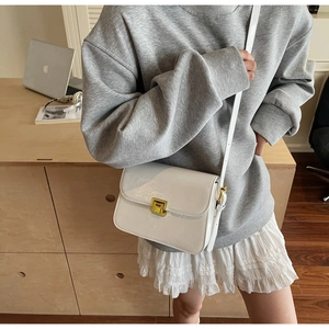 Detailed view of glossy white patent leather crossbody bag with square gold metal clasp