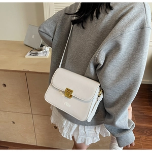Detail of white patent leather shoulder bag with gold rotating lock and long strap