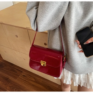 Detail of a deep red patent leather shoulder bag with a gold metal lock worn by a model