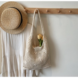 Detailed texture of hand-woven beige crochet beach bag with hollow mesh on a wooden hook