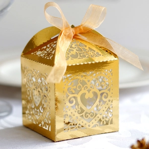 Detailed laser-cut heart pattern on gold favor box with elegant champagne ribbon bow
