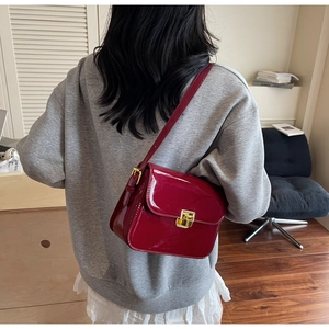Detail of red patent leather shoulder bag featuring a gold square metallic lock clasp