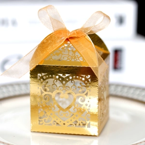 Close-up of golden hollow heart wedding candy box with elegant silk ribbon on white plate