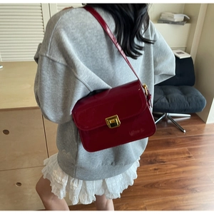 Side view of a glossy red patent leather crossbody bag with a gold buckle on a model